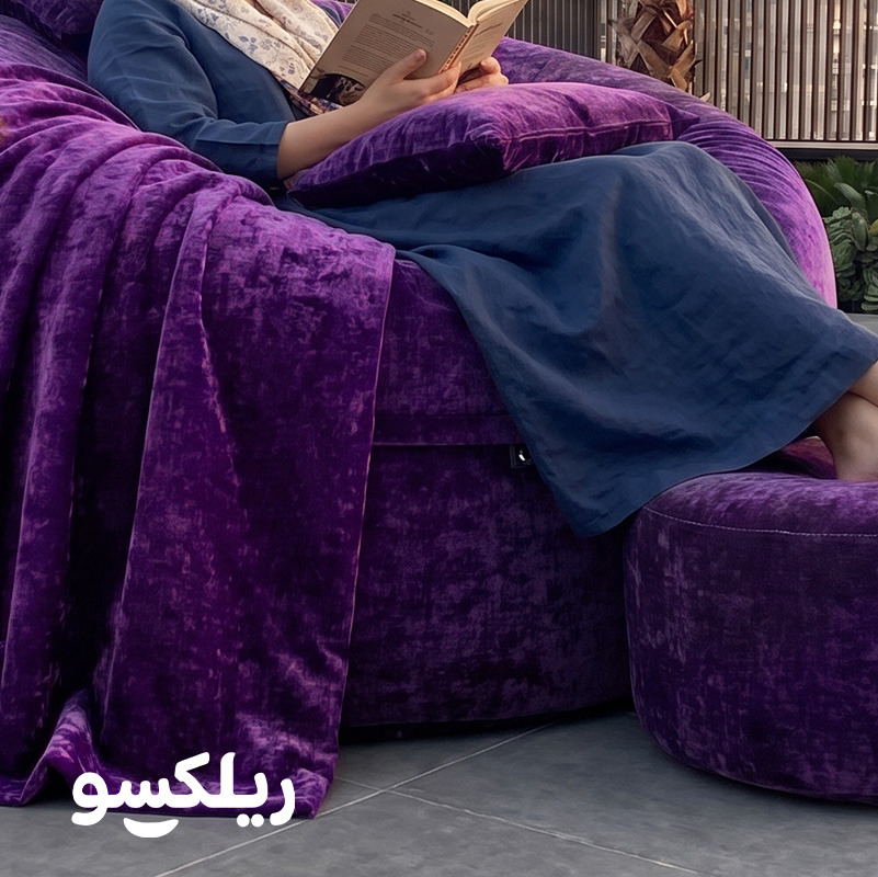 خانم در حال استفاده از بین بگ لاکچری مخملی بنفش ریلکسو با کتاب — مبل شنی با زیرپایی